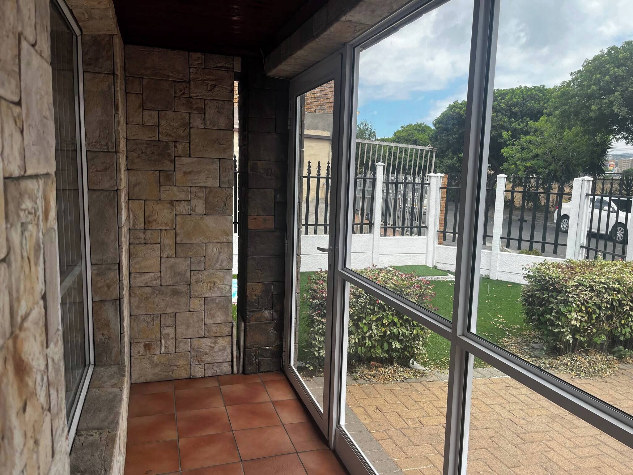 A balcony with stone walls and a view of a gated area with greenery.