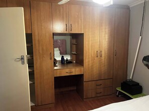 A wooden wardrobe with a mirror, a desk with a chair, and a bedside table with a lamp. - Serene Guest Room Retreat Near Cape Town Airport (Cape Town)