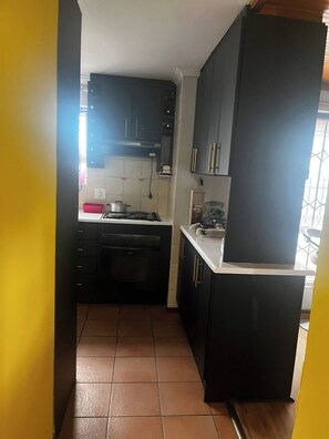 A compact kitchen with dark cabinets, a stove, and a small countertop. - Serene Guest Room Retreat Near Cape Town Airport (Cape Town)