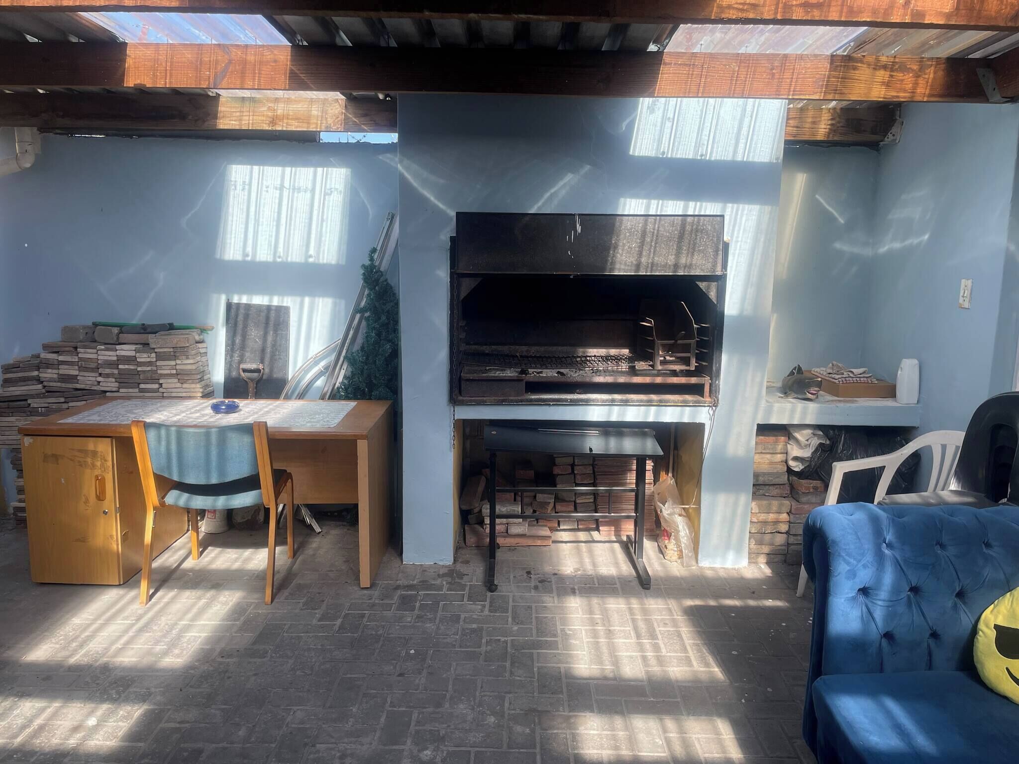 A patio area with a brick floor, a wooden table with chairs, a blue sofa, and a fireplace.