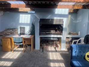 Un espace patio avec un sol en briques, une table en bois avec des chaises, un canapé bleu et une cheminée.