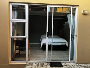 Une pièce comprenant un lit, une chaise et une porte-fenêtre coulissante donnant sur un espace extérieur.