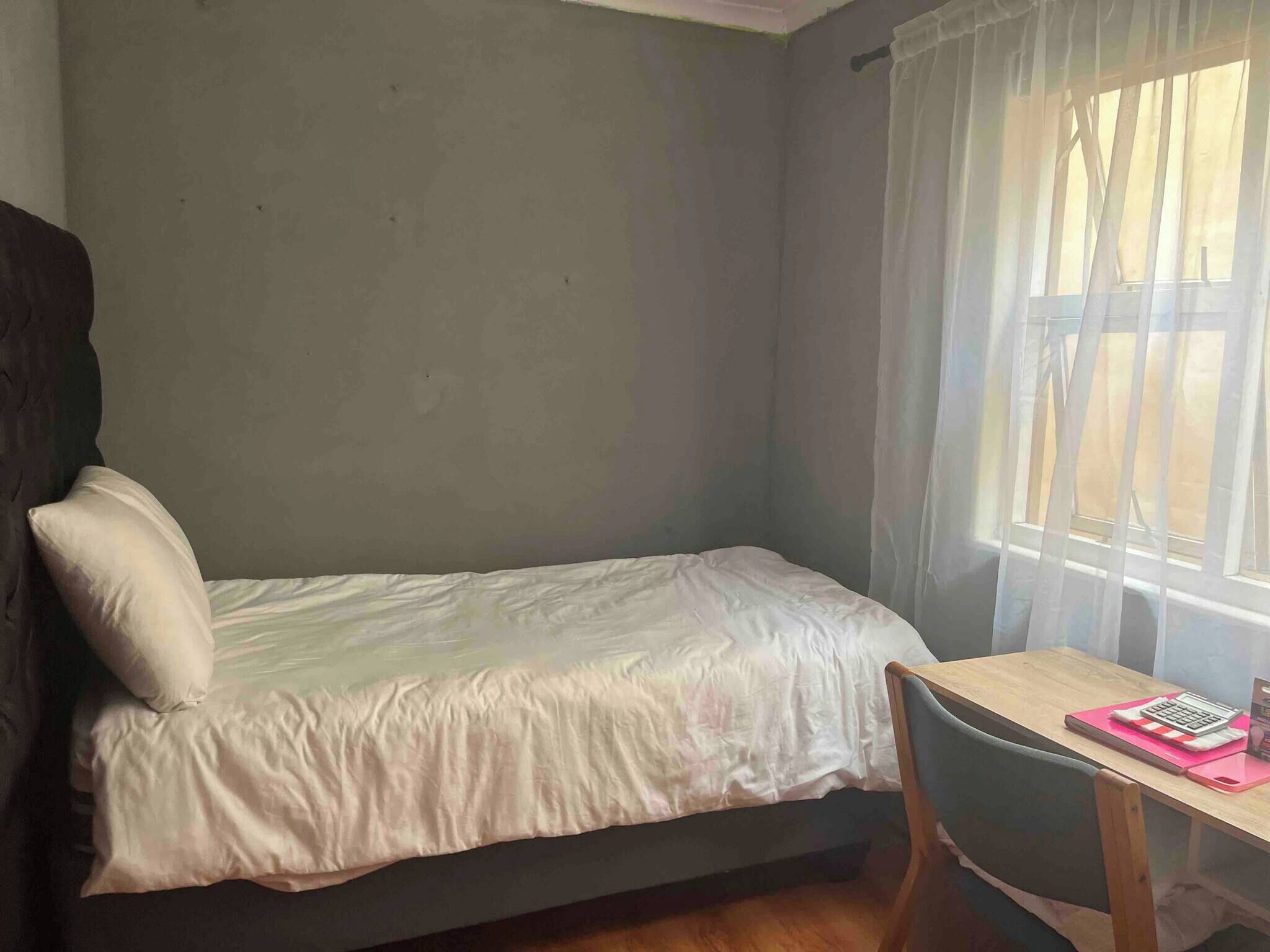 A small room with a bed, a chair, a table, and a window with curtains.