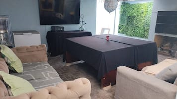 Una habitación con mesa de billar, sofás, televisor y pared verde.