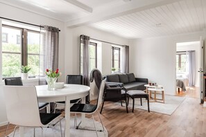 A modern living room with a dining area, large windows, and a view of greenery outside. - Linneby , fri parkering (Uddevalla)