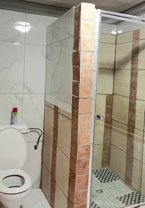 A bathroom with a toilet, a shower enclosure, and a tiled floor.