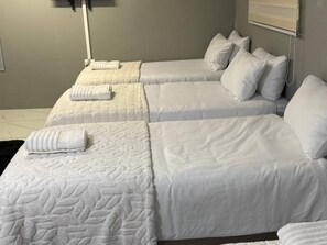 Una camera d'albergo con due letti, ciascuno con una coperta e dei cuscini bianchi, e un tappeto nero.
