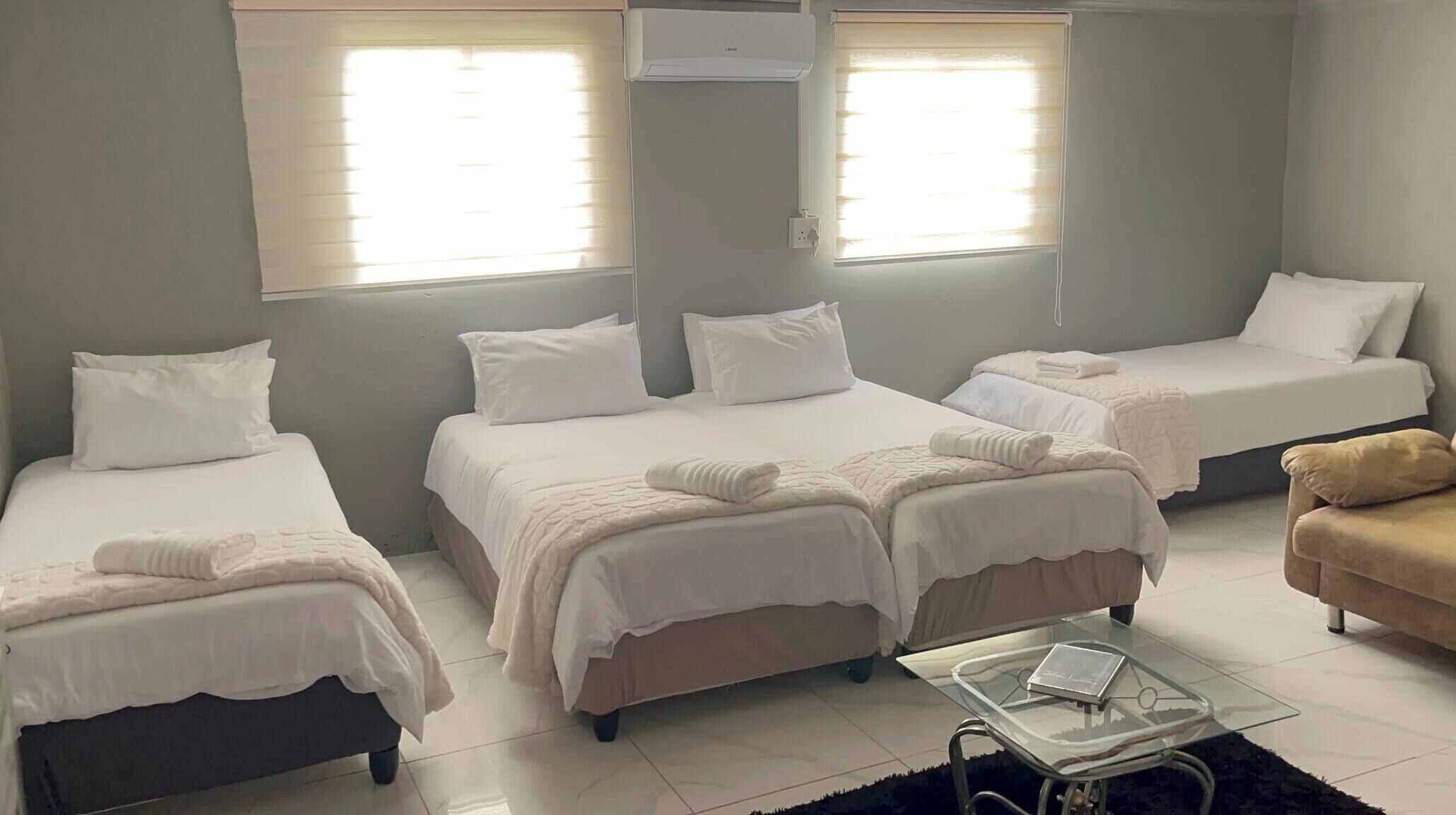 Habitación de hotel con tres camas, un sofá, una mesa de centro de vidrio y un equipo de aire acondicionado.
