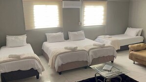 A hotel room with three beds, a sofa, a glass coffee table, and an air conditioning unit.