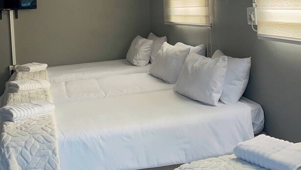 A room with a bed, a bedside table, a wall-mounted TV, and a window with blinds.