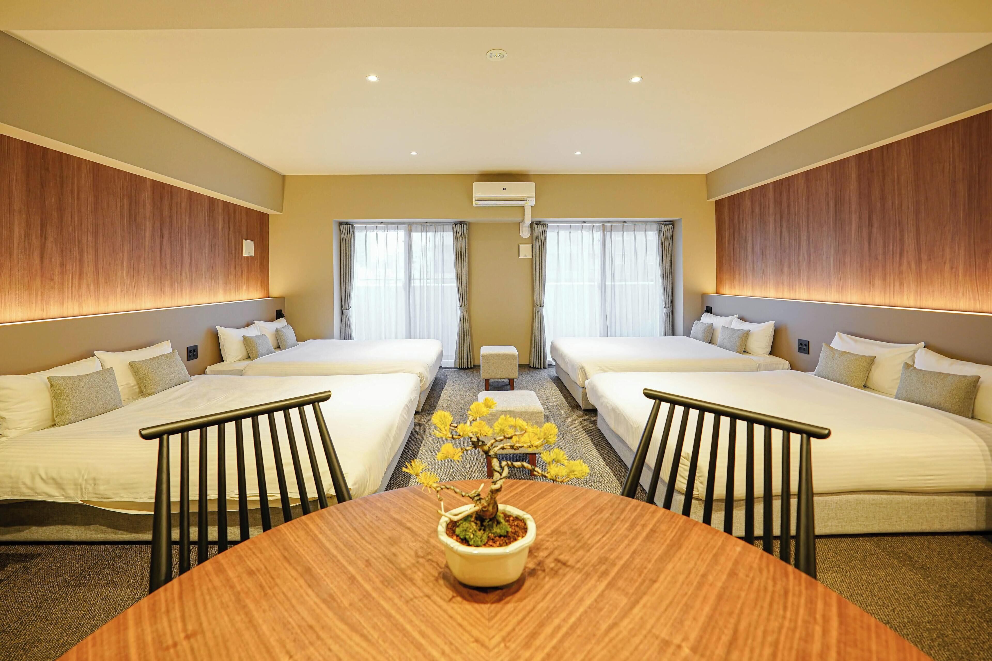 A hotel room with two beds, a round table with a potted plant, and an air conditioning unit on the wall.