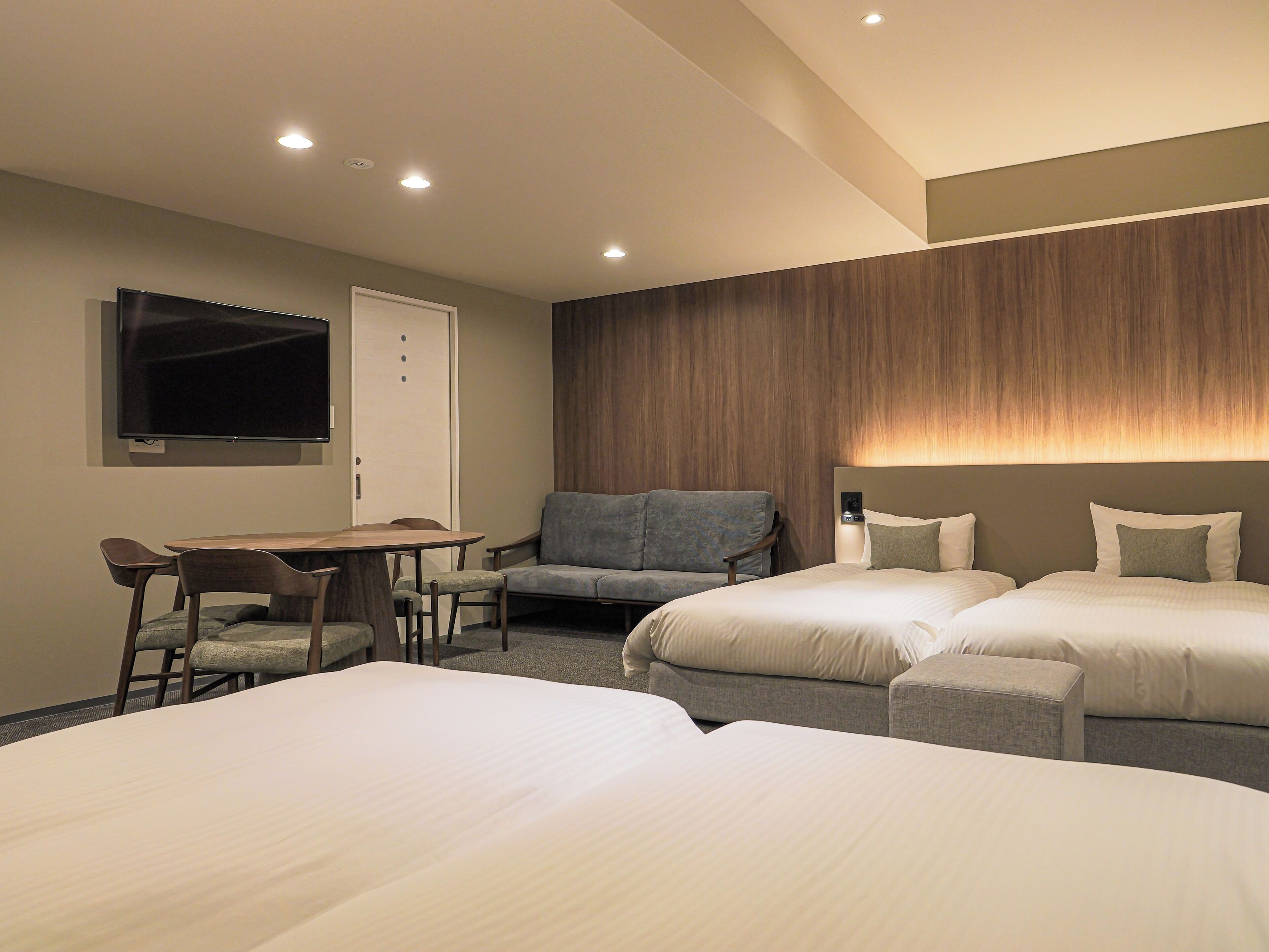 Une chambre d’hôtel avec deux lits, un bureau, une chaise, une télévision et un lampadaire fixé au mur.
