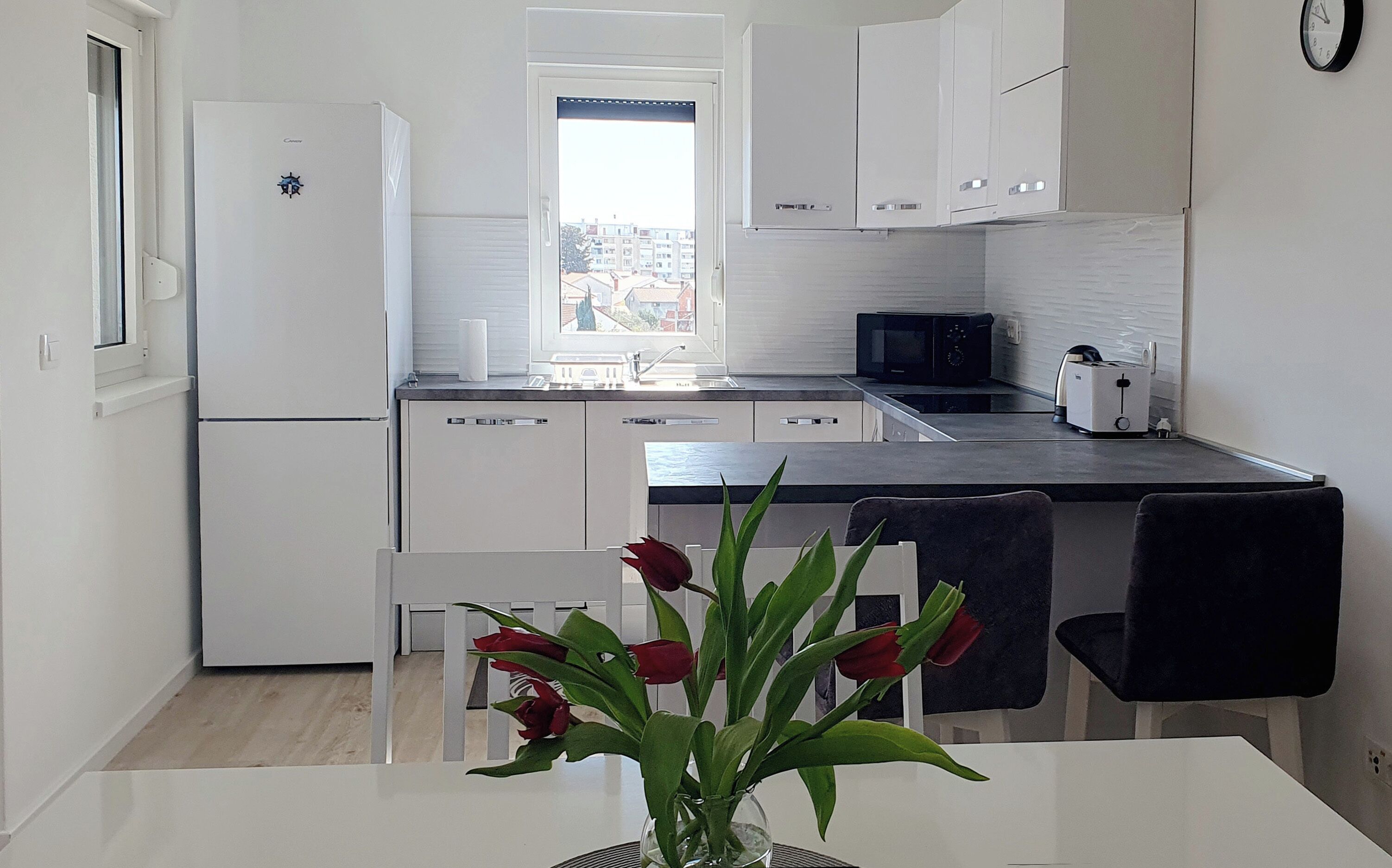 Una cocina moderna con armarios blancos, encimera negra y vistas por la ventana.
