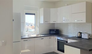 A modern kitchen with white cabinets, a built-in microwave, and a view of the city through a window. - Apartment Dino, Zadar - Charming Fully Furnished 2-Bedroom with AC (Zadar)