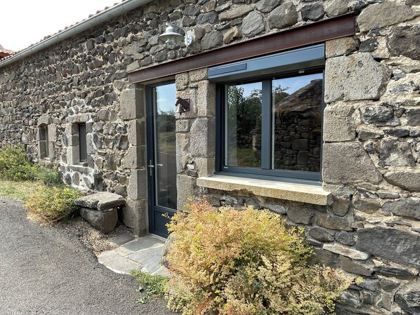 Un edificio de piedra con una puerta oscura, ventanas y un alero de piedra.