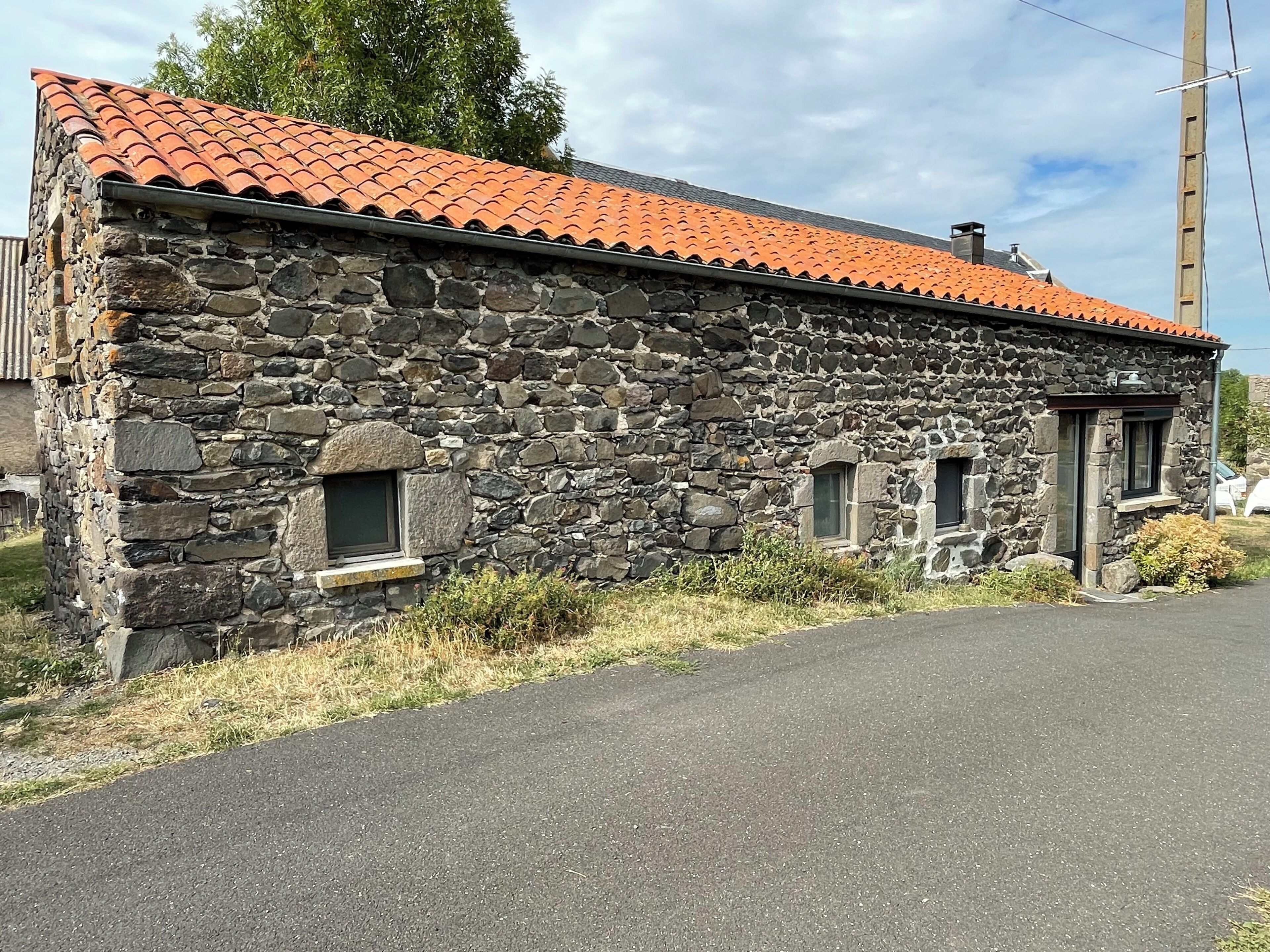 Ein Steinhaus mit rotem Ziegeldach, zwei kleinen Fenstern und einer gepflasterten Auffahrt.