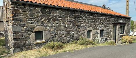 Un bâtiment en pierre avec un toit recouvert de tuiles rouges, deux petites fenêtres et une allée pavée.