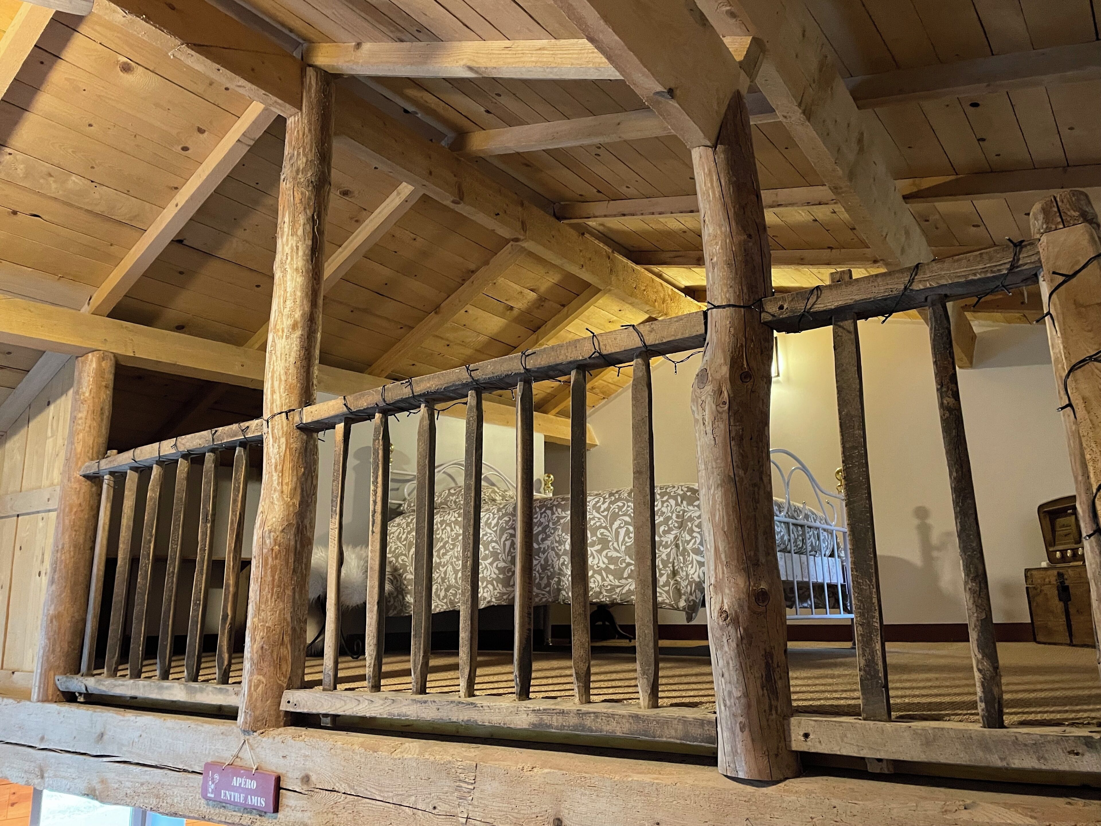 Un balcon en bois avec une balustrade en métal, des poutres en bois et un lit avec une literie à motifs.