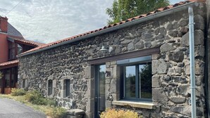A stone building with a red-tiled roof, a large window, and a stone wall.