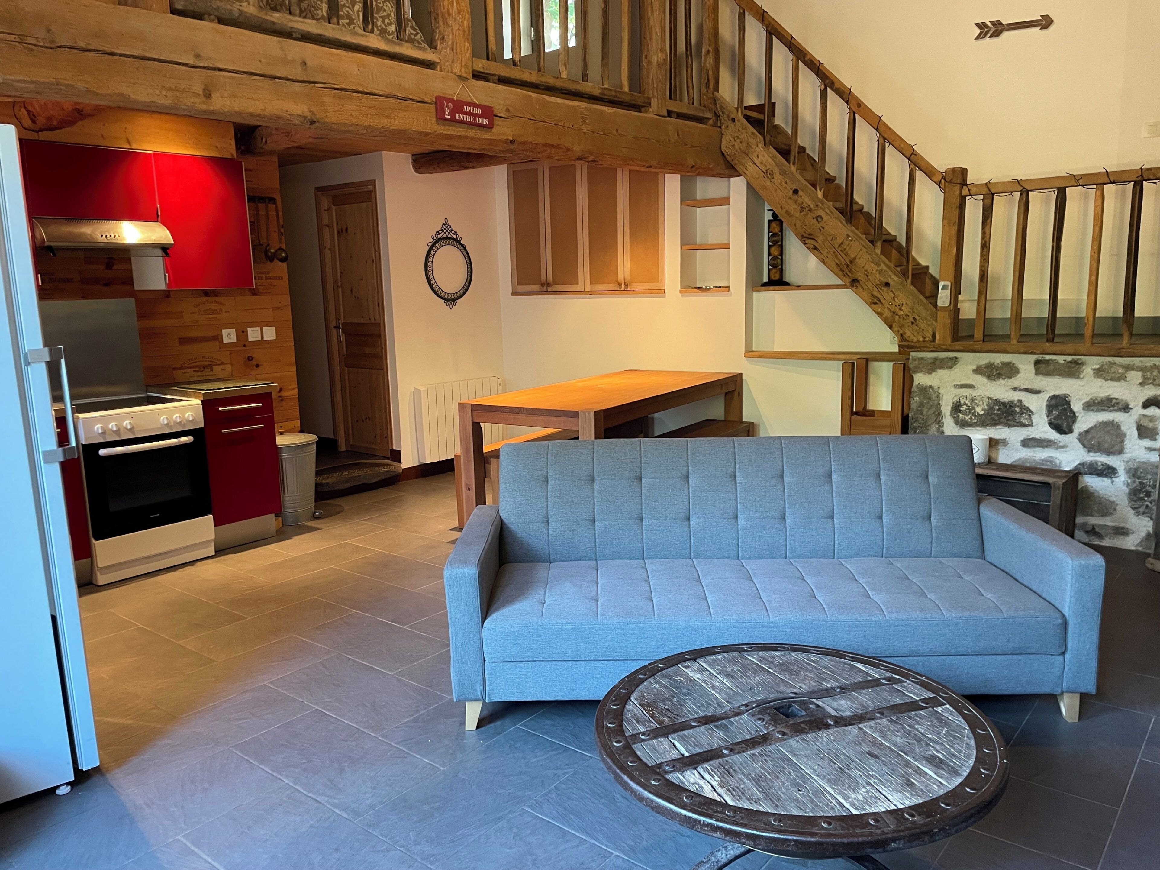 Een zithoek met een bank, een ronde tafel, een keuken met rode kasten en een houten trap.
