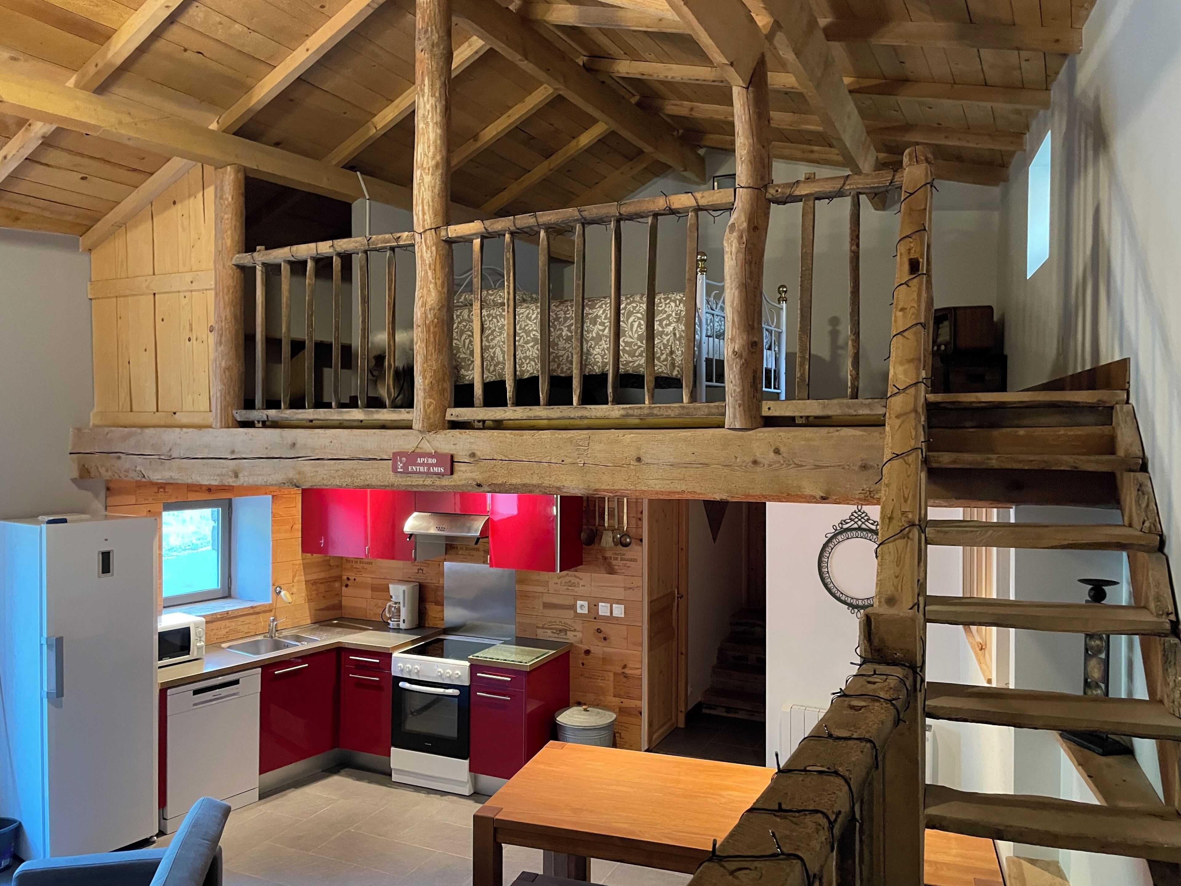 A loft bedroom with a wooden ceiling, a small kitchen area, and a staircase leading to an upper level.