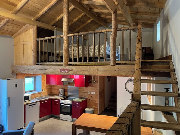 A loft bedroom with a wooden ceiling, a small kitchen area, and a staircase leading to an upper level.