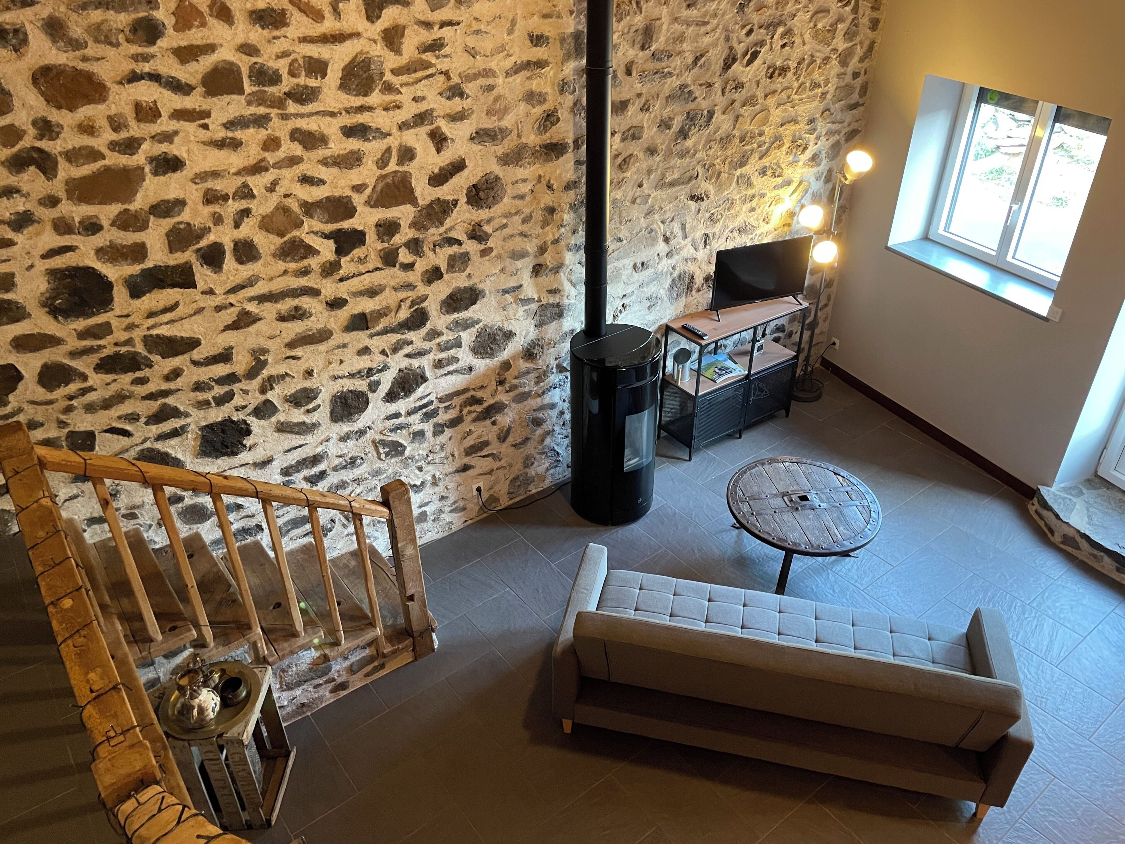 Interior con pared de piedra, un sofá, una mesa y una escalera de madera.