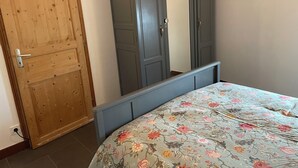 A bedroom with a wooden door, a grey wardrobe, and a bed with a floral bedspread.