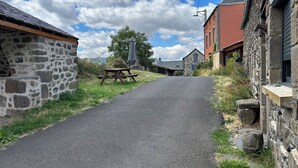 A narrow paved road flanked by stone buildings, a picnic table, and a lamp post.
