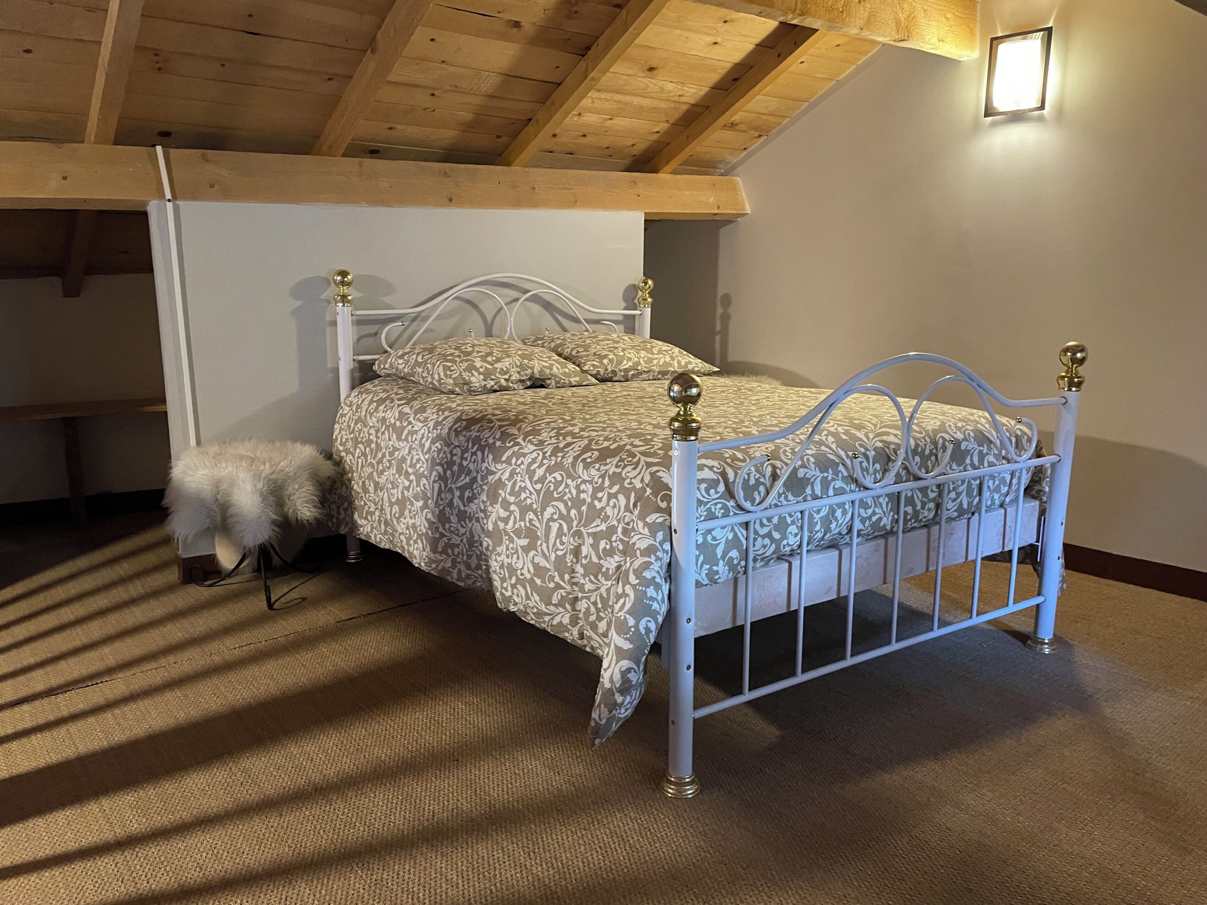 Ein Schlafzimmer mit einem Bettgestell aus weißem Metall, einer gemusterten Tagesdecke und einem kleinen, weißen, flauschigen Sessel.