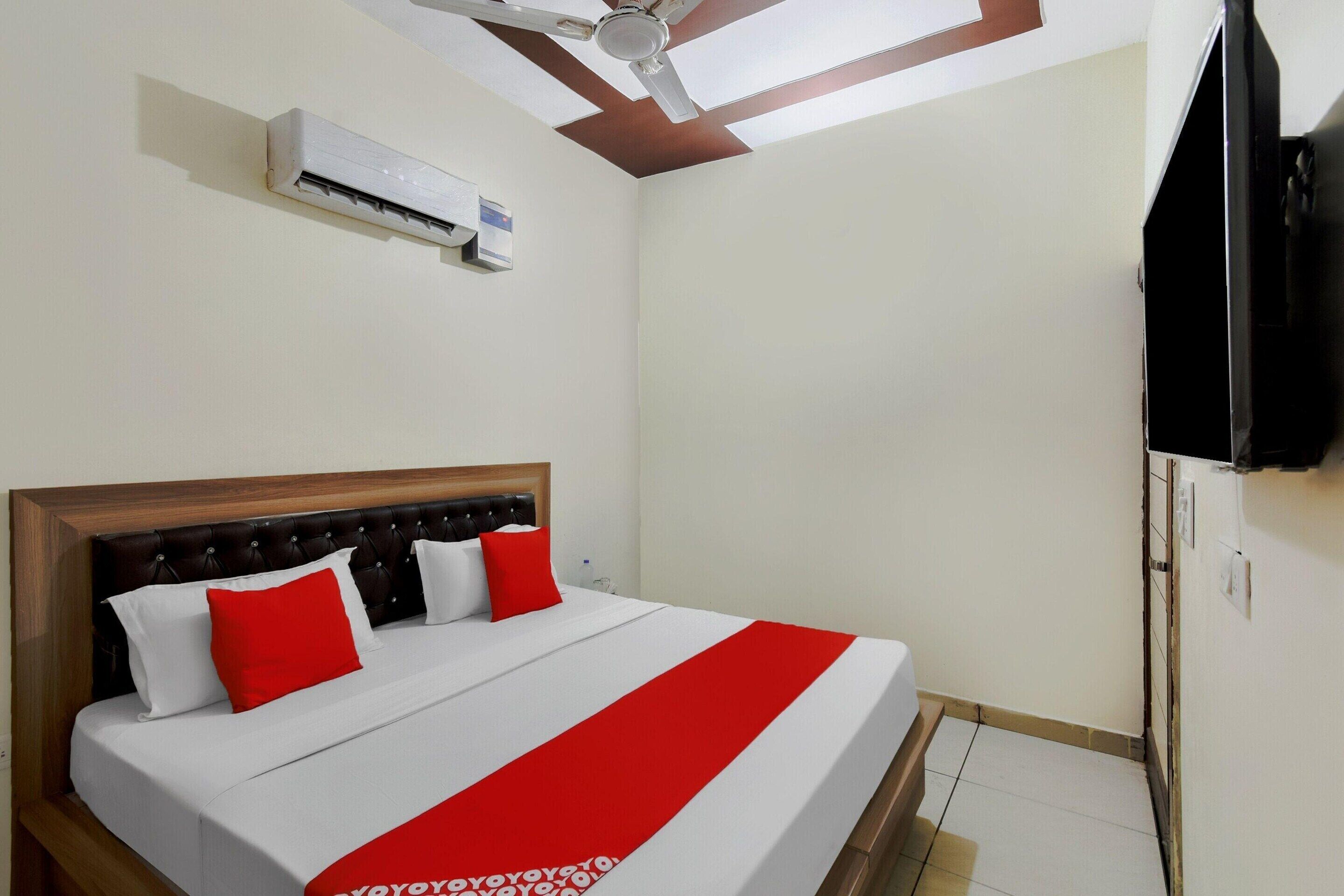A hotel room with a bed, a ceiling fan, an air conditioning unit, and a television.