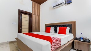 A hotel room with a bed, a bedside table, a water bottle, and a phone. - Deluxe Hotel Amigo (Thanesar)