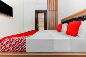 A hotel room with a bed, a television mounted on the wall, and a door leading to the bathroom. - Deluxe Hotel Amigo (Thanesar)
