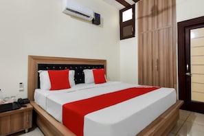 A hotel room with a bed, a wardrobe, a bedside table, and an air conditioning unit.