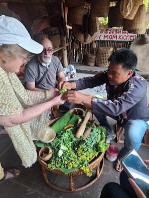 A group of people preparing food outdoors with a basket of vegetables and a sign that reads 'Mom Kitchen.'