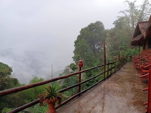 A pathway with a railing, surrounded by lush greenery and a thatched-roof structure.