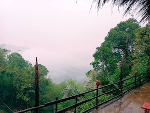 A wooden railing with a view of a lush green forest and mist-covered mountains.