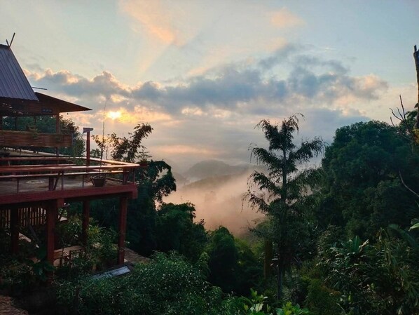Une structure en bois dotée d’un balcon donnant sur un paysage luxuriant et surmontée d’une chaîne de montagnes brumeuse.