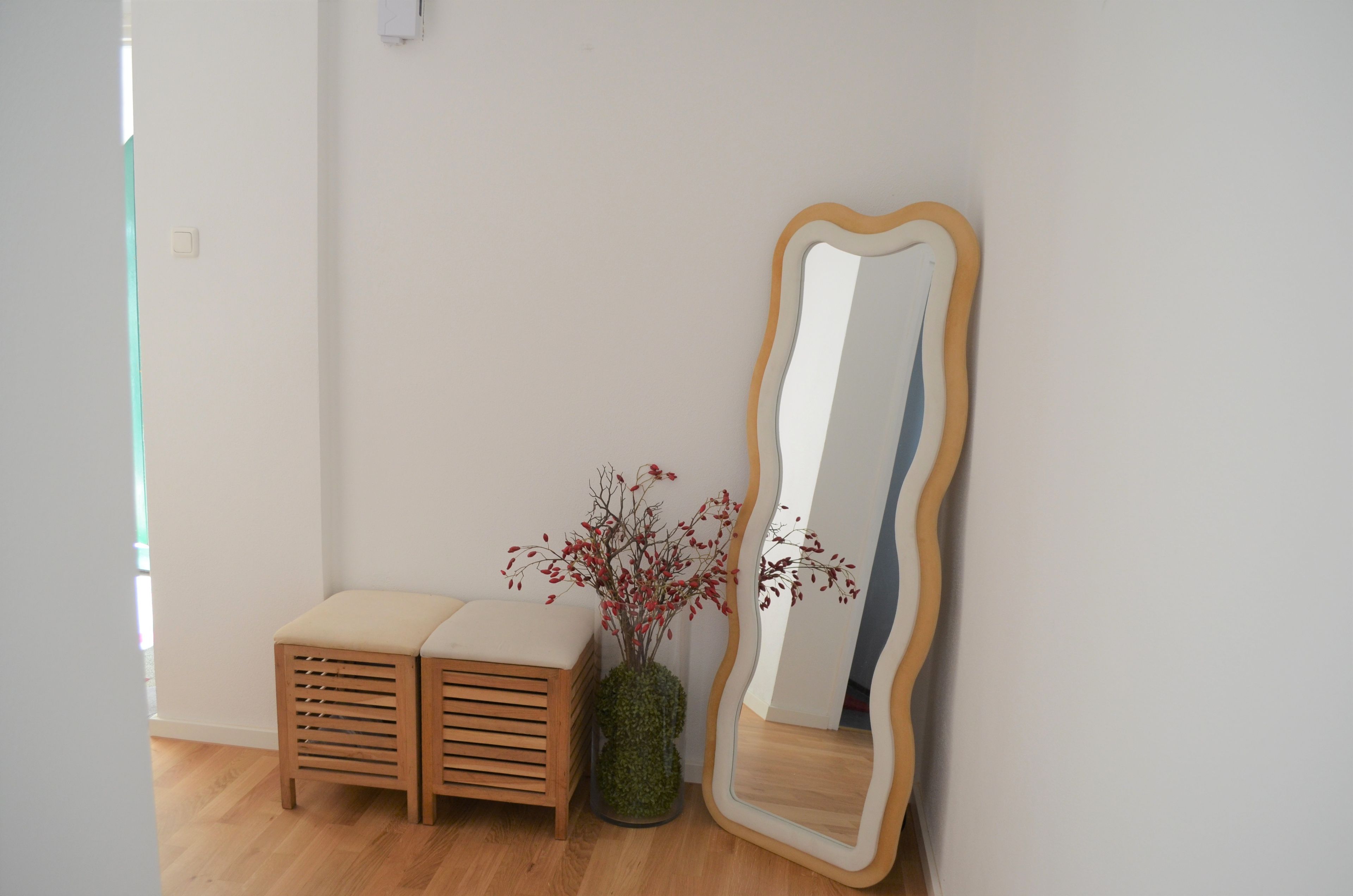 A room with a wooden bench, a large mirror with a wooden frame, and a vase with red berries.