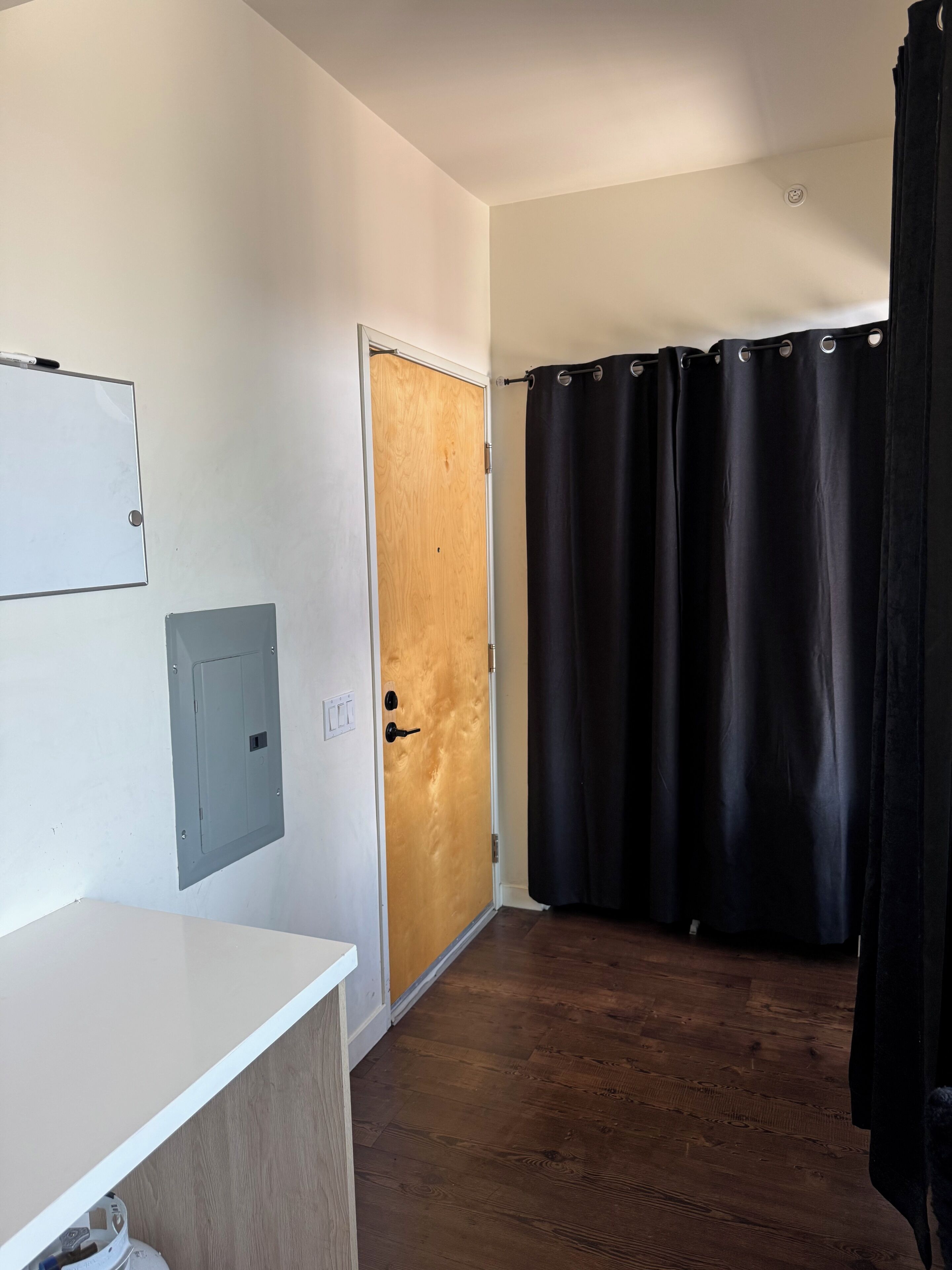 A hallway with a wooden door, a black curtain, a white wall with a light switch, and a white counter.