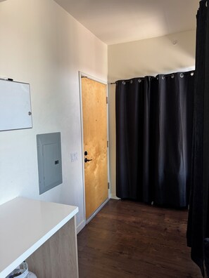 A hallway with a wooden door, a black curtain, a white wall with a light switch, and a white counter. - Modern Studio with balcony in the center of Hollywood Walk of Fame area (Los Angeles)