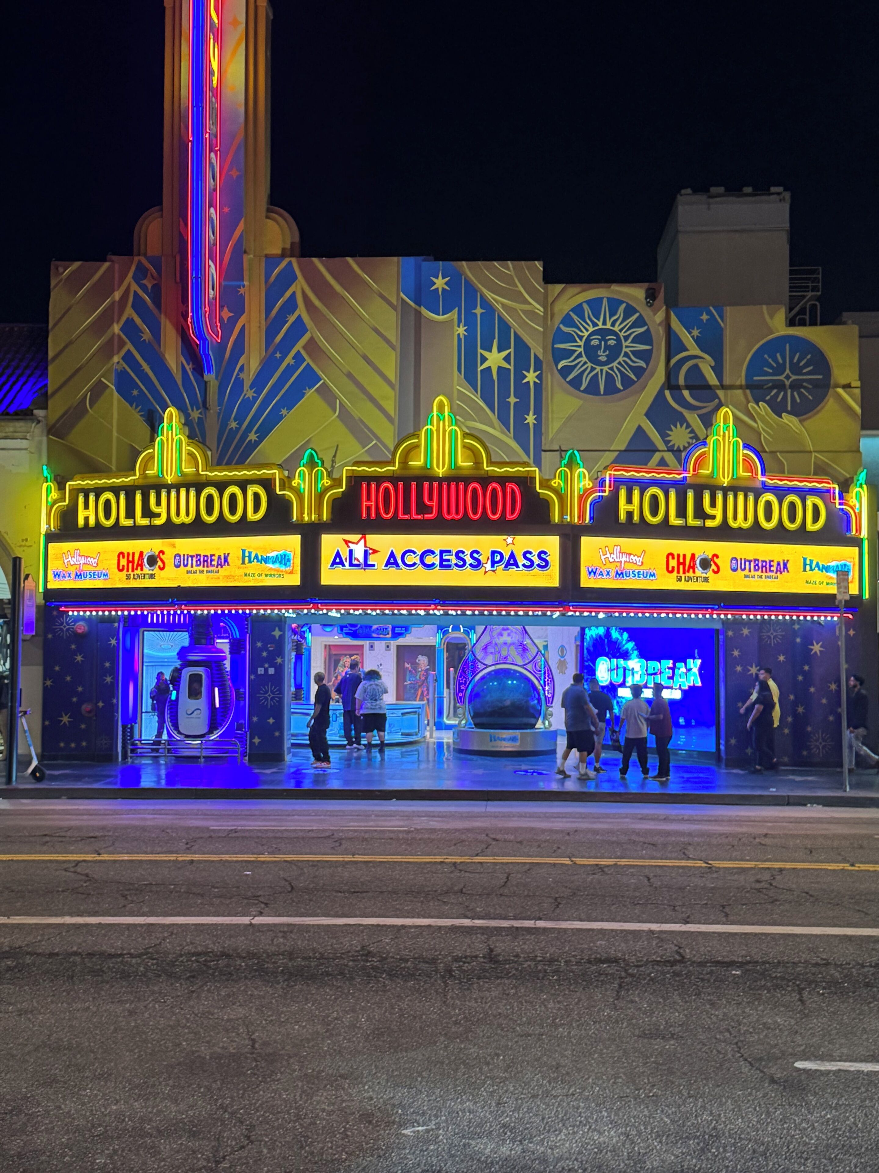 Um edifício bem iluminado com letreiros de neon que dizem 'HOLLYWOOD' e 'ALL ACCESS PASS'.