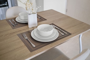A dining table set with white plates, bowls, and cutlery. - Arova by Kozystay - Cilandak (South Jakarta)