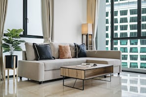 A modern living room with a sectional sofa, a coffee table, a floor lamp, and a potted plant. - Arova by Kozystay - Cilandak (South Jakarta)
