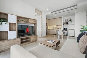 Ein modernes Wohnzimmer mit Fernseher, einer Couch, einem Couchtisch und einer Küche im Hintergrund.