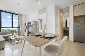 A modern dining area with a wooden table, white chairs, and a view of the city through large windows. - Arova by Kozystay - Cilandak (South Jakarta)