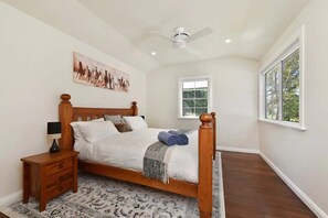A bedroom with a wooden bed, a nightstand, a ceiling fan, a window, and a wall-mounted painting. - Laguna Farmhouse Estate (Laguna)