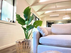 A modern living room with a sofa, a large green plant, and a wicker basket. - Laguna Farmhouse Estate (Laguna)