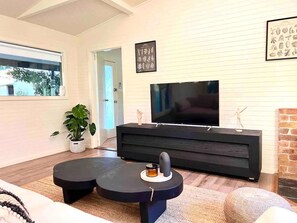 A modern living room with a flat-screen TV, a black entertainment unit, a potted plant, and a large window. - Laguna  Farmhouse Studio (Laguna)