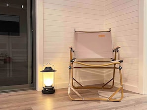 A corner room with a wooden floor, a white wall, and a folding chair with a label.